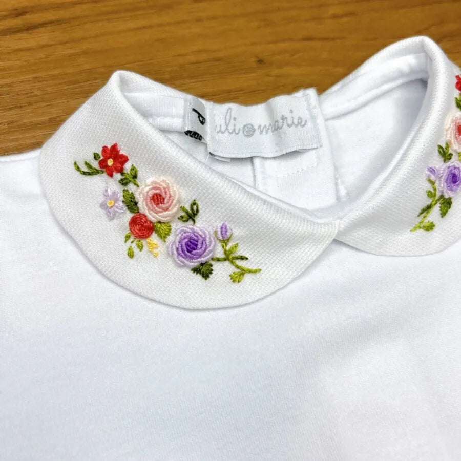 body lilac, modelo branco com gola bordada em flores coloridas nos tons de lilás, rosa e verde, confeccionado em algodão macio para o máximo conforto do bebê