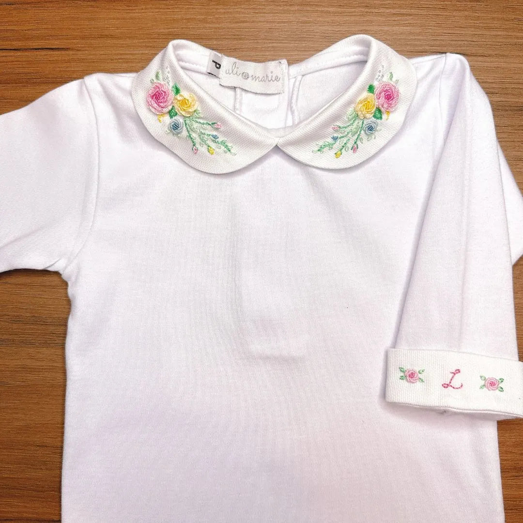 body martina branco em malha de algodão com gola redonda bordada com flores coloridas, sobre fundo de madeira