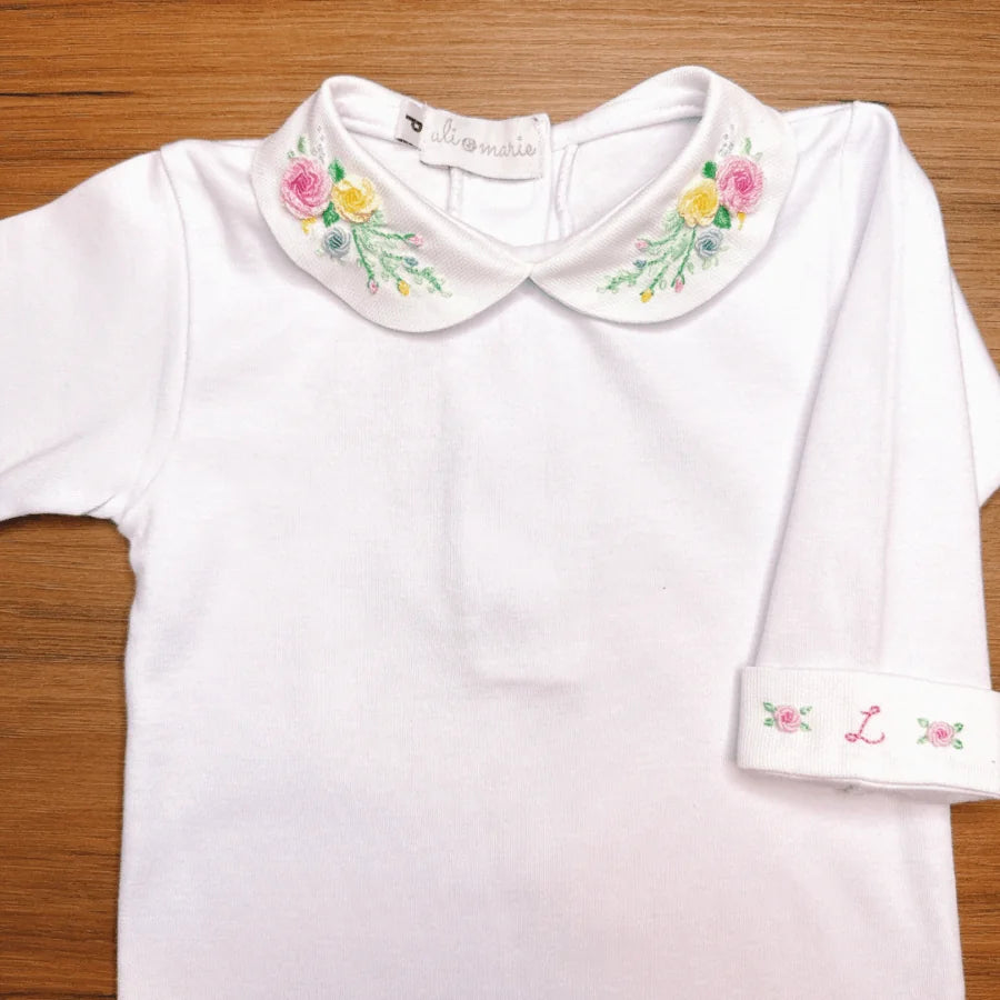 body martina branco em malha de algodão com gola redonda bordada com flores coloridas, sobre fundo de madeira