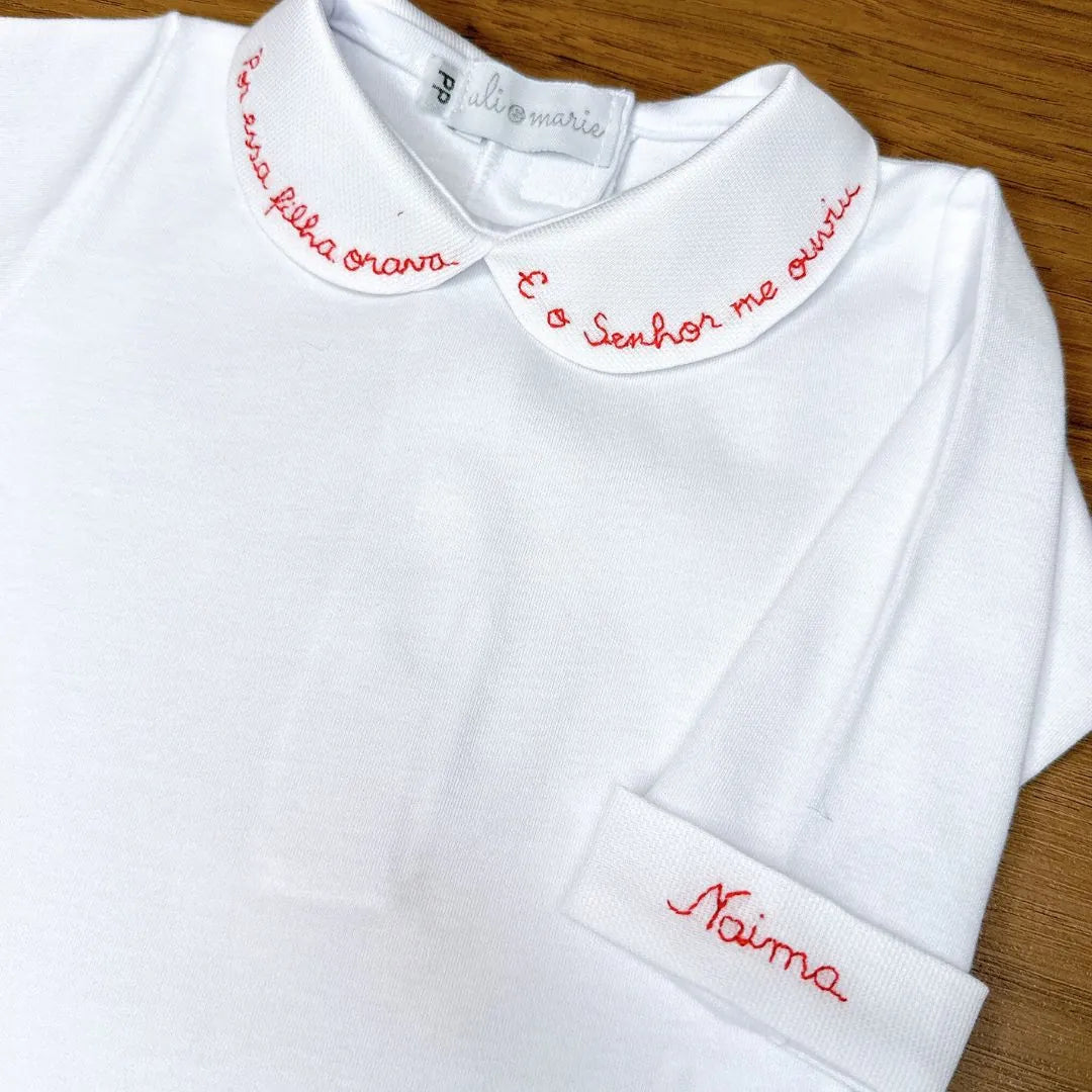 body milagre branco com gola peter pan bordada em vermelho com frase religiosa e detalhe de botão vermelho no punho
