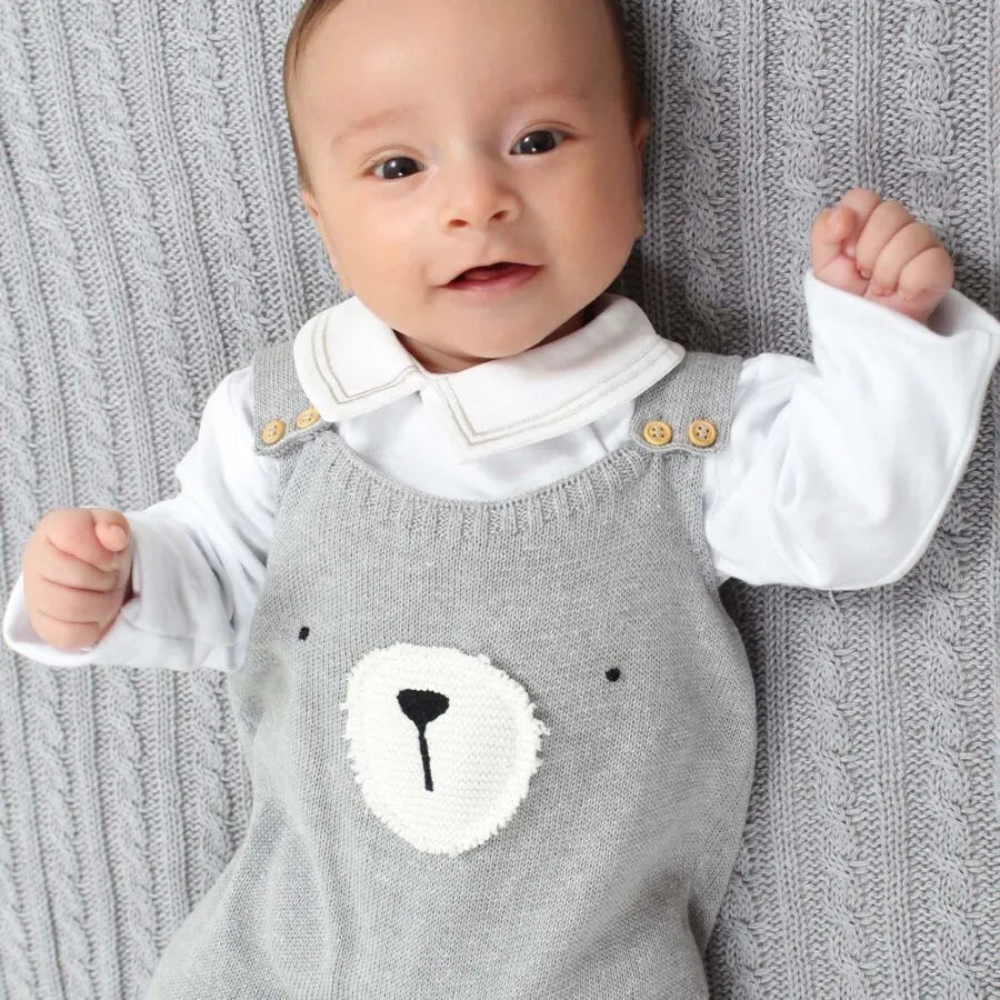 jardineira teddy cinza de tricô com body branco de manga longa, detalhe de rosto de urso bordado no peito