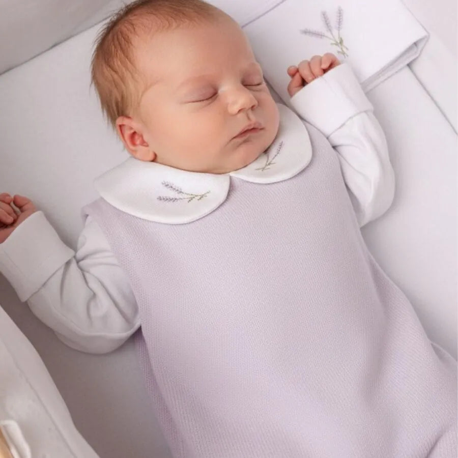 bebê dormindo confortavelmente usando a jardineira de tricô lavanda com body branco e gola bordada com raminhos de lavanda