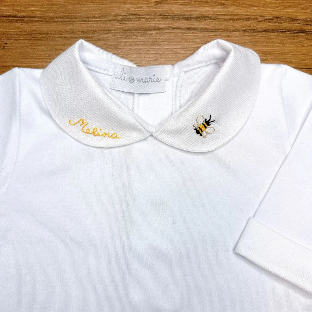 close-up da gola piquet do body branco com a abelhinha e nome 'melina' bordados em destaque