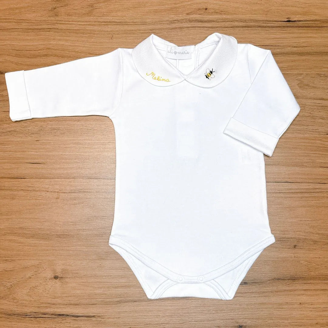 body manga longa branco do kit baby bee personalizado, exibindo a gola com o nome 'melina' e bordado de abelha