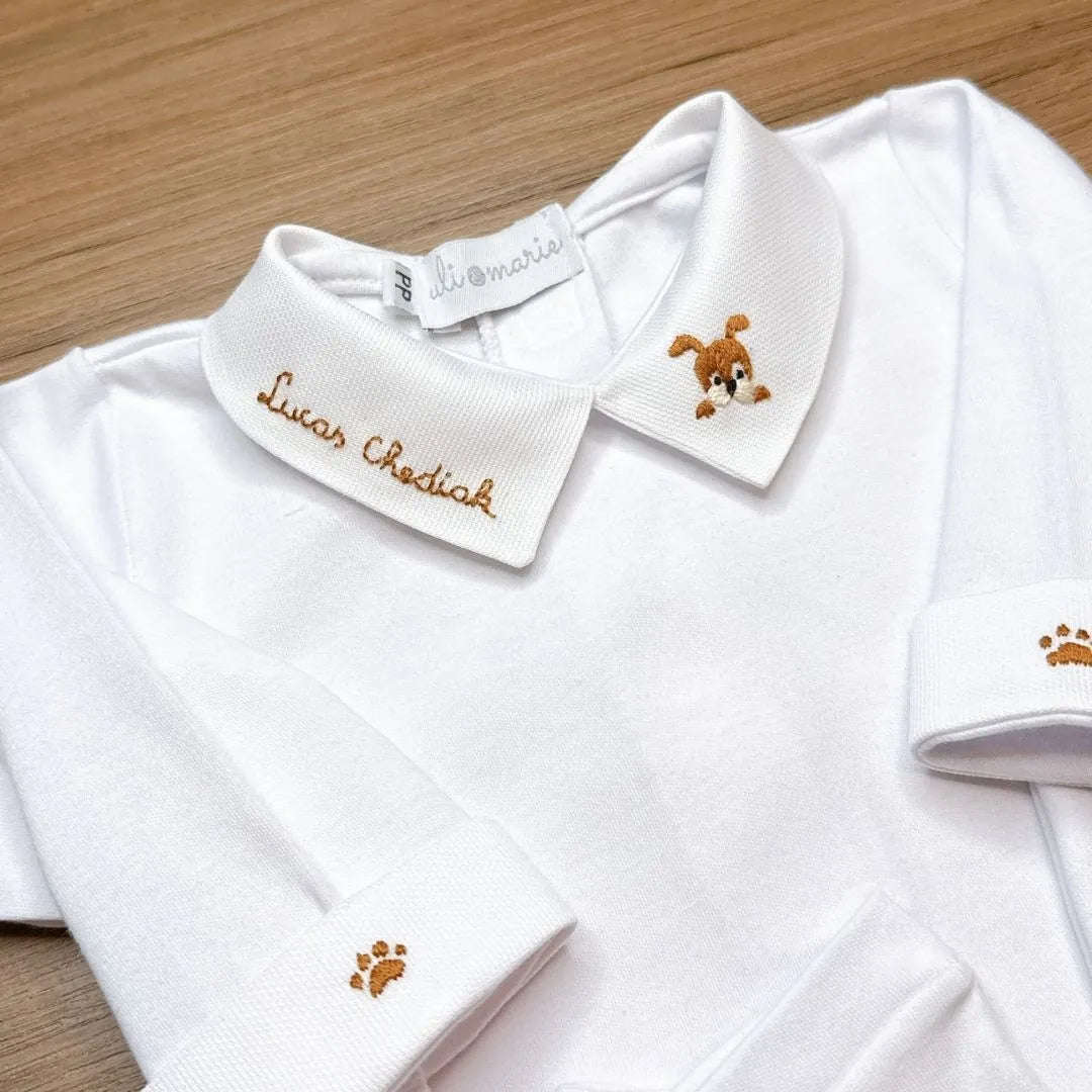 detalhe do bordado de cachorrinho na gola do body branco com nome 'lucas chediak' e pata no punho dobrado