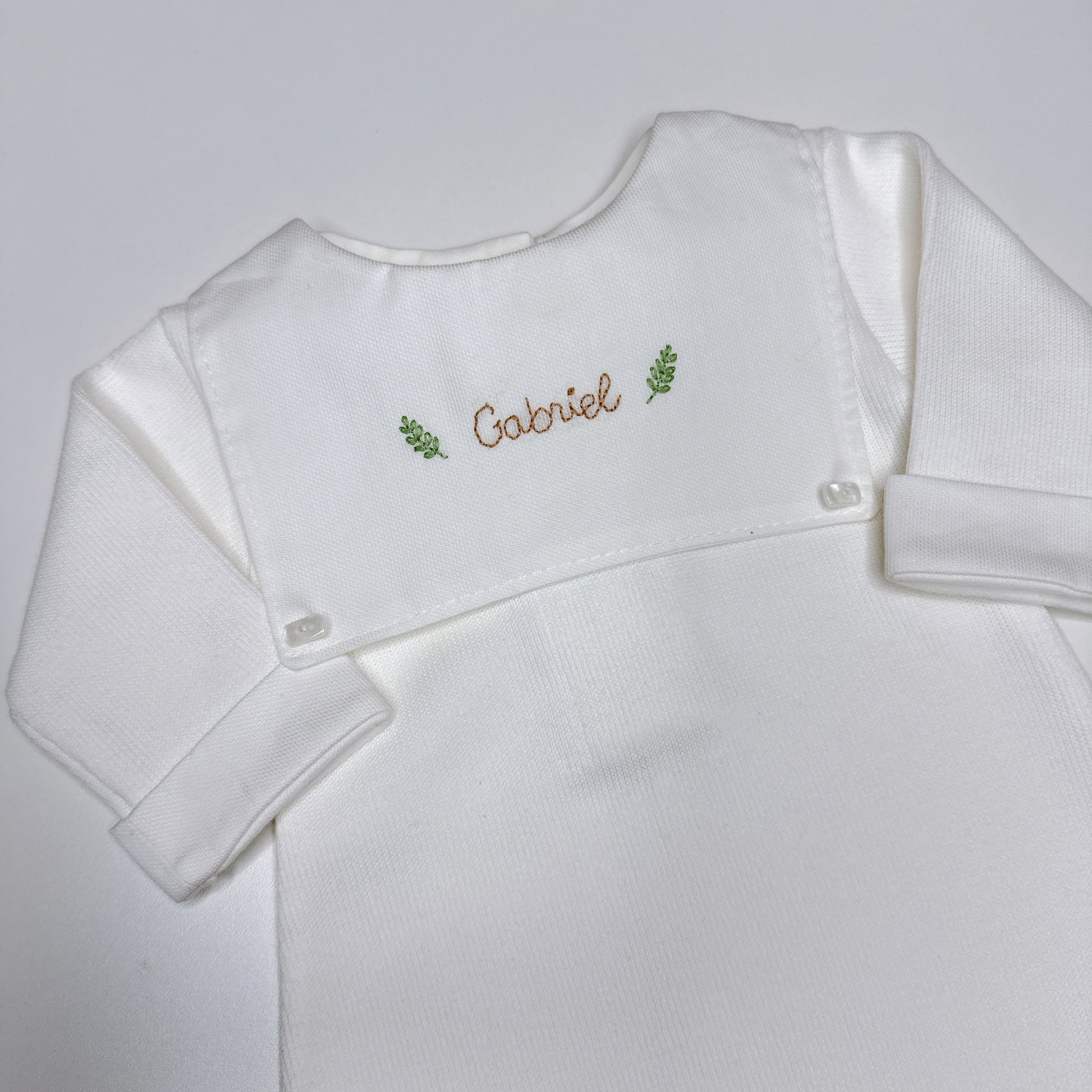 Macacão Luiz personalizado branco com pala frontal e nome Gabriel bordado em marrom com ramos verdes