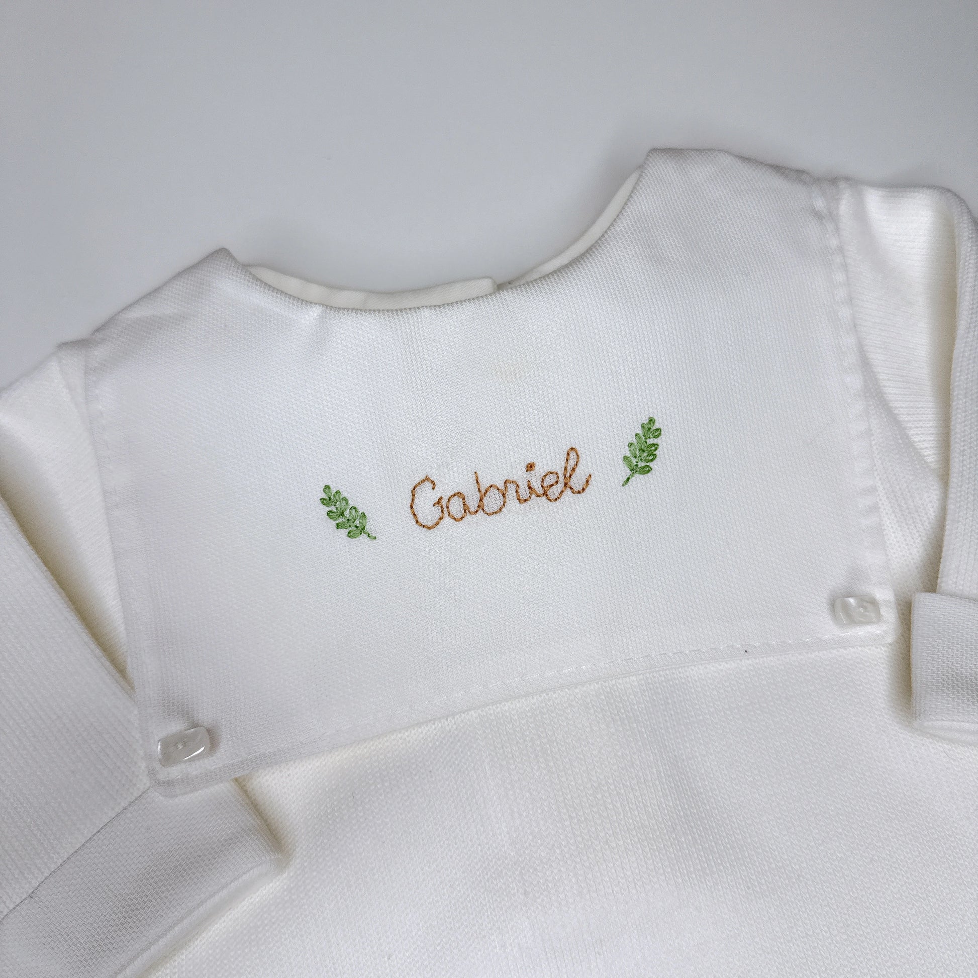 Macacão Luiz personalizado branco com pala frontal e nome Gabriel bordado em marrom com ramos verdes