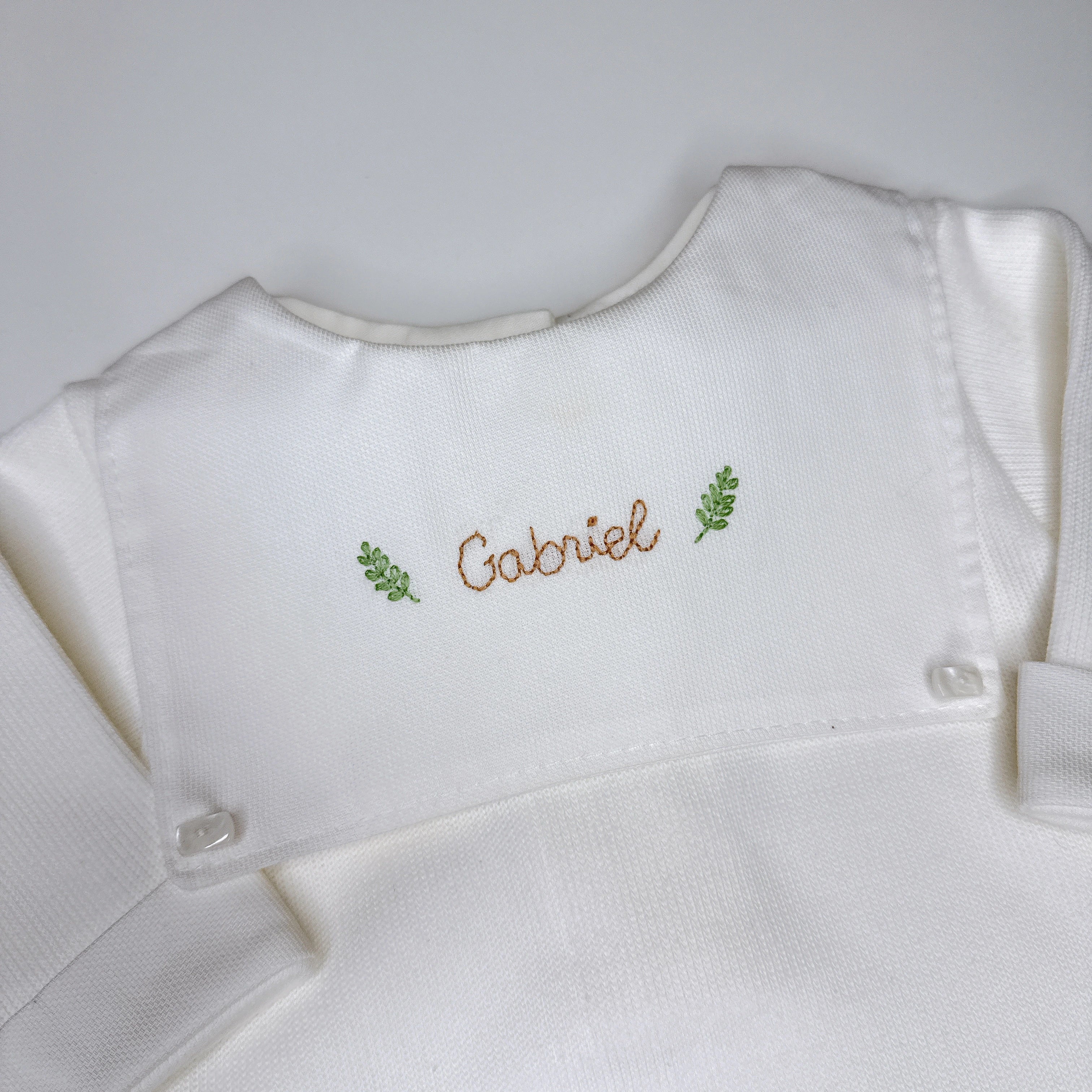 Macacão Luiz personalizado branco com pala frontal e nome Gabriel bordado em marrom com ramos verdes