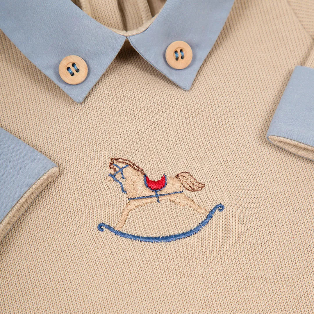 close-up do bordado detalhado do cavalo de balanço no peito do macacão horse, com destaque para os botões de madeira da gola