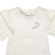 macacão laura off-white canelado em suedine com babador bordado com flores e punho virado, botão de pressão frontal