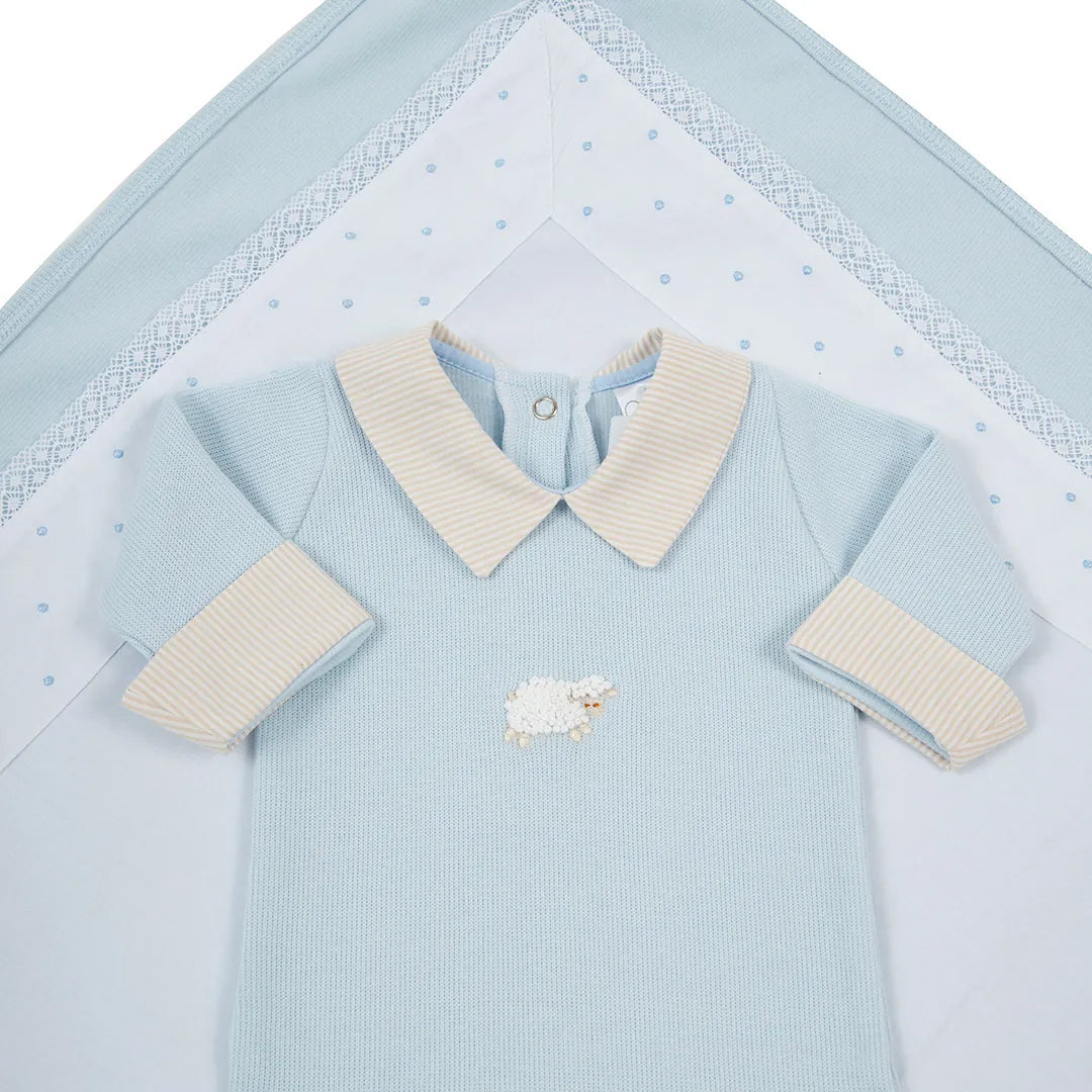 macacão ovelha em algodão azul bebê com bordado de ovelha branca, com gola e punhos listrados, exibido sobre a manta