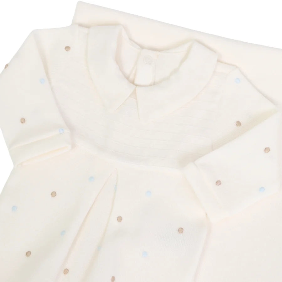 Detalhe do macacão off-white com poás azuis e bege, gola e pala em tecido liso, sobre a manta do conjunto