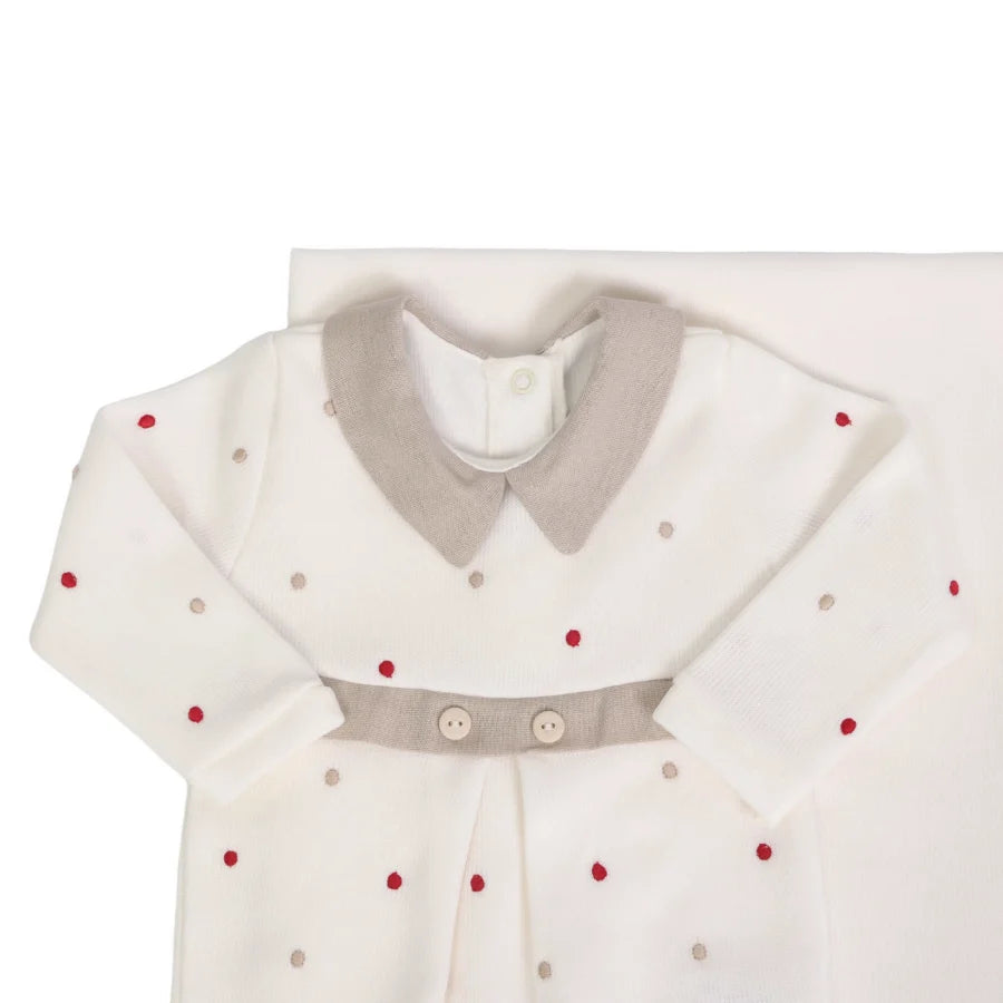 Detalhe do macacão off-white com gola e faixa bege, decorado com poás bege e vermelhos, sobre a manta do conjunto