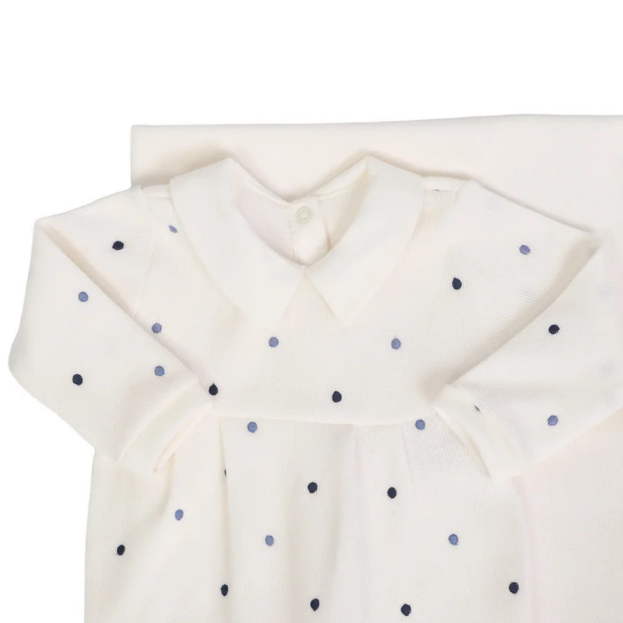 Detalhe do macacão off-white com gola clássica e poás bordados em azul marinho e azul claro, sobre a manta do conjunto