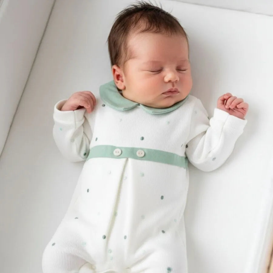 Bebê usando o macacão Theo verde off-white: gola verde, faixa com botões, poás verdes e cinzas em fundo off-white