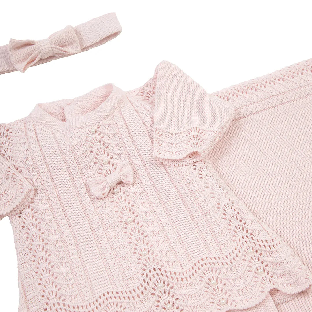 close-up do vestido de tricô rosa bebê com estampa rendada, laço delicado e manta combinando ao fundo